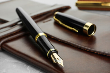 Stylish fountain pen, cap and leather notebook on light grey table, closeup