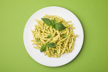 Plate of delicious trofie pasta with pesto sauce and basil leaves on light green table, top view