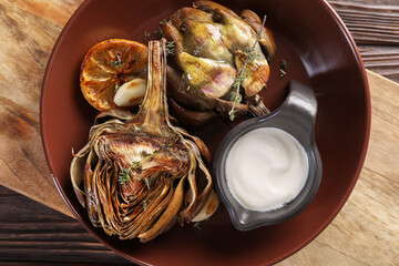 Tasty grilled artichoke and sauce in bowl on wooden table, top view
