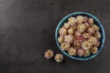 Bowl with dried strawflowers on grey table, flat lay. Space for text