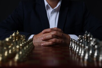 Man with chess pieces on board before game against dark background, closeup - Powered by Adobe