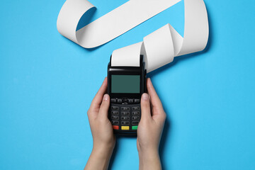Woman using payment terminal with thermal paper for receipt on light blue background, top view