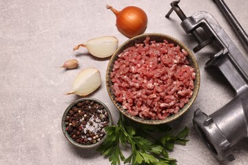 Manual meat grinder with beef mince, peppercorns, onion and parsley on light grey table, flat lay
