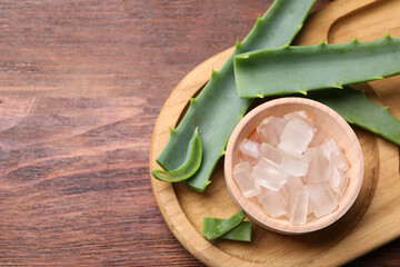 Aloe vera gel and slices of plant on wooden table, flat lay. Space for text
