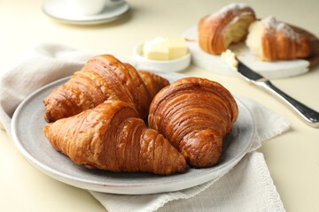 Plate with tasty croissants on beige table, closeup