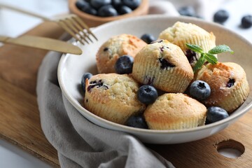 Delicious muffins with blueberries and mint in bowl on table, closeup