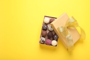 Open box with delicious chocolate candies on yellow background, top view. Space for text