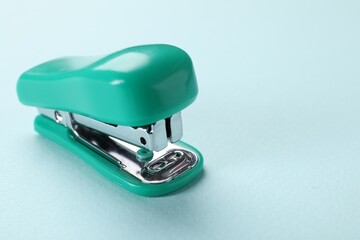 Turquoise stapler on light blue background, closeup. Space for text