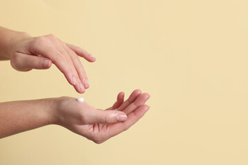Woman applying cosmetic cream onto hand on beige background, closeup. Space for text