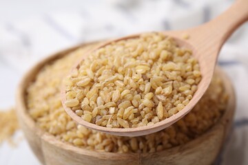 Taking raw bulgur with spoon from bowl on table, closeup