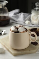 Cup of aromatic hot chocolate with marshmallows and cocoa powder on white wooden table