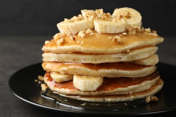 Delicious pancakes with bananas, walnuts and honey on dark table, closeup