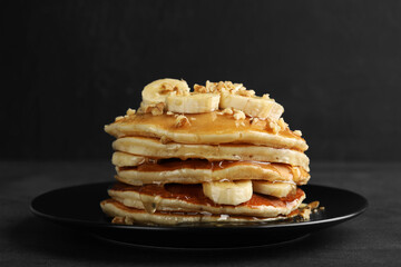 Delicious pancakes with bananas, walnuts and honey on dark table, closeup