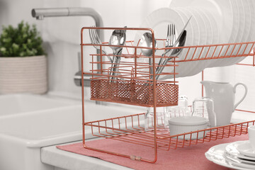 Drying rack with clean dishes and cutlery on countertop near sink in kitchen