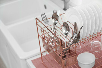 Drying rack with clean dishes and cutlery on countertop near sink in kitchen