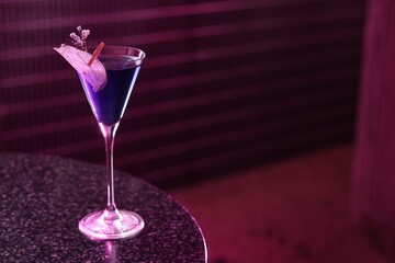 Fresh alcoholic cocktail in glass on table against dark purple background. Space for text