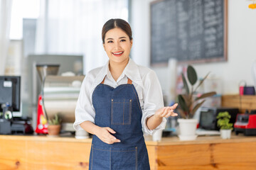 Opening a small business, AHappy Asian woman in an apron standing near a bar counter coffee shop,...