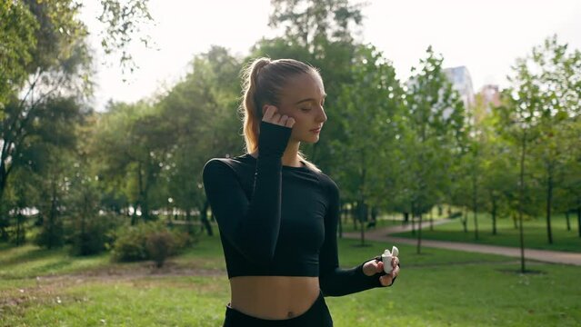 portrait of a young beautiful girl in sportswear in a city park putting on headphones before starting sports training