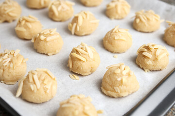Many almond flour cookie in rows on parchment paper, ready to be baked. Gluten free unbaked raw cookie dough. Group of round cookie dough balls with almond slices. GF almond cookies. Selective focus.