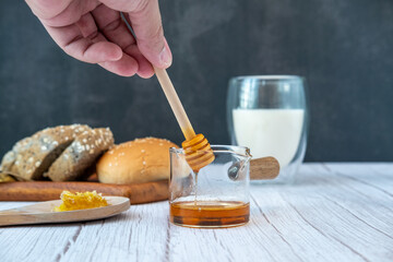 Male hands are using a stick for stirring honey in a measuring cup with bread and milk.