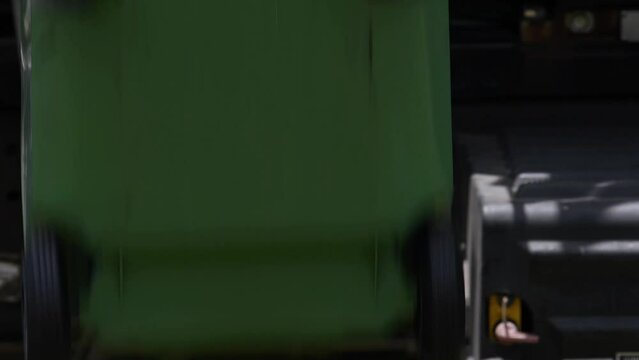 Close-up green rubbish garbage trash bin can picked up emptied out collection truck lorry semi driving out of shot 