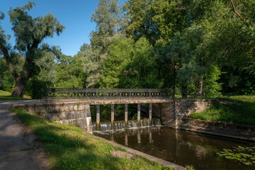 Fototapeta na wymiar Slavyanka River and the Black Bridge in the Pavlovsk Palace and Park Complex on a sunny summer day, Pavlovsk, Saint Petersburg, Russia