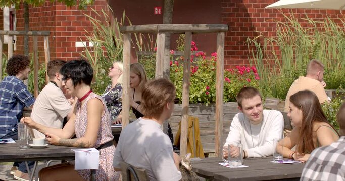 A group of people sitting at a table, hanging out and talking on a sunny weekend day. New acquaintances, energy of community communication.