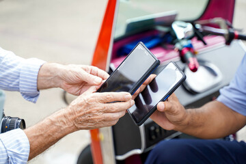 Closeup and crop hands of senior tourist paying the fare to the Tuktuk Thailand taxi driver by smart phone.