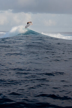 Sunset surfer on a wave in Tahiti in the deep blue ocean water