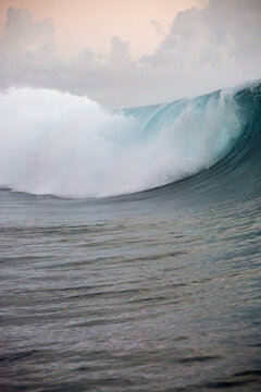 A beautiful blue wave of water turns for a surfer to surf it in Tahiti 