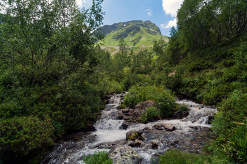 View of the Malaya Dukka River against the backdrop of the mountains of the North Caucasus on a sunny summer day, Arkhyz, Karachay-Cherkessia, Russia © Ula Ulachka