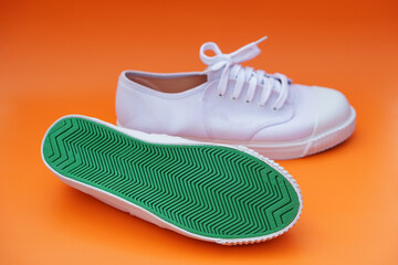 Pair of new white canvas sneakers, one shows green rubber under the shoes , orange background. Comfortable, fashionable. Concept, shoes for doing sport or exercise also can wear for traveling, hiking.
