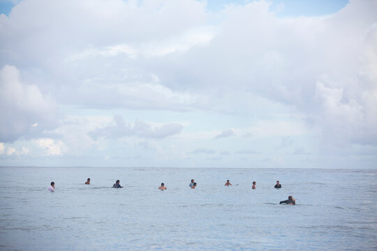 Surfers wait in the water with their backs turned to camera in Tahiti on the ocean