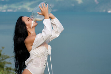 Sexy woman in lingerie drink milk from can and bottle against countryside. Sexy woman drinking milk...