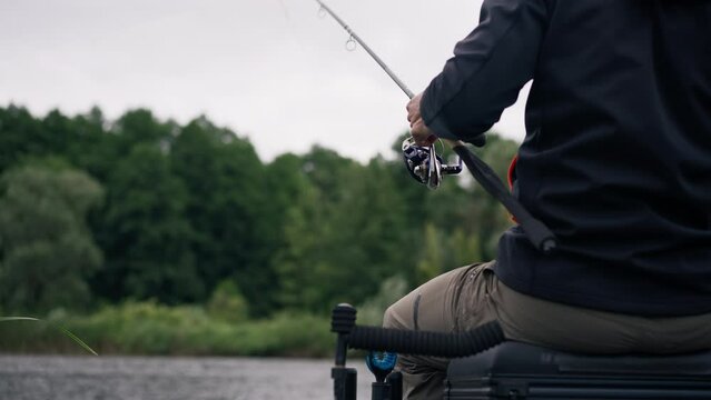 close up Fisherman with fishing rod or spinning and professional tools sitting on the river bank rear view Pull fish out of the lake sports fishing