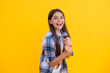 smiling young girl singer perform karaoke isolated on yellow background. With microphone in hand teenage girl singer. young karaoke singer girl hold microphone. teen girl singer hold mic in studio - obrazy, fototapety, plakaty