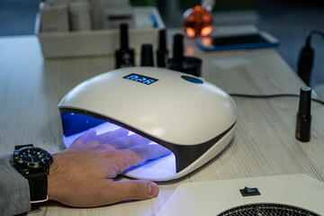 Man hand lies in an ultraviolet lamp with blue shining in room. Men's manicure procedure in a...