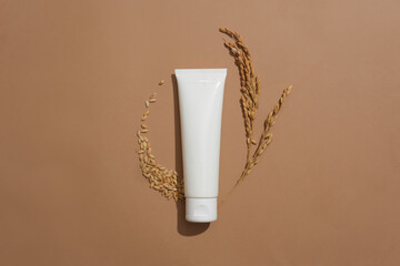 An unlabeled lotion tube and whole grain rice on a brown background. Rice bran extract contains many nutrients and antioxidants that help brighten skin and limit melasma.