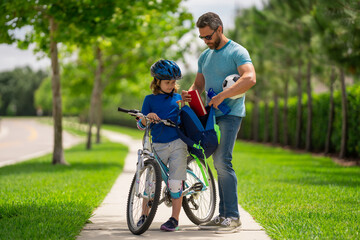 Fototapeta premium Father helping son get ready for school. Father teaching son cycling. Father and son learning to ride a bicycle at Fathers day. Father support and helping son. Child care.