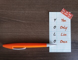 On wood copy space background, Pen with text written note You Only Live Once - concept of YOLO - ideology is an encouragement to seize the day, to go for it, live your best life now