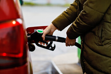 Close-up of hands of woman at self-service gas station, hold fuel nozzle and refuel the car with...