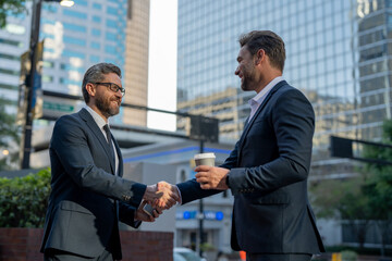 American businessman shaking hands with partner. Businessmen in suit shaking hands outdoors. Handshake between two businessmen. wo business men had business contacts. Business strategy.