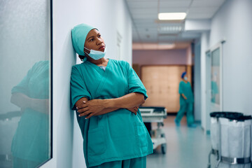 Pensive black female surgeon in hospital hallway.