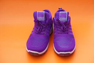 Pair of new purple sneakers. Fashionable and comfortable sport footwears. Orange background. Concept, shoes for doing sport or exercise also can wear for traveling, hiking.