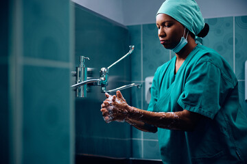 Black surgeon washing her hands before operation at clinic. - obrazy, fototapety, plakaty