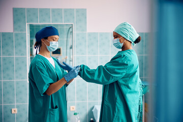 Black female doctor preparing for surgery with help of nurse in operating room.