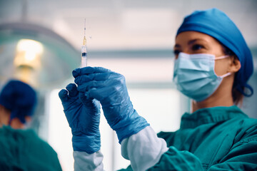 Close up of surgical nurse preparing syringe in operating room.