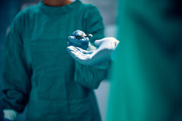 Close up of nurse handing surgical instrument to surgeon in operating room.