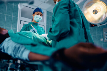 Female doctor performing surgical procedure on patient in operating room. - obrazy, fototapety, plakaty