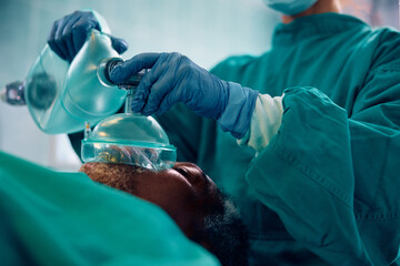 Close up of anesthesiologist using oxygen mask on patient during surgery in operating room.